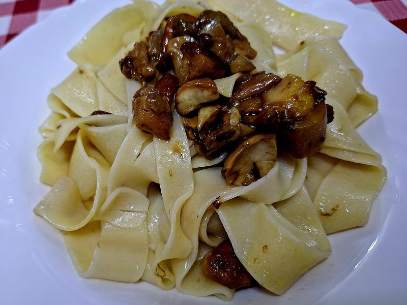 Pappardelle largos servidos com fatias douradas de cogumelo por cima.