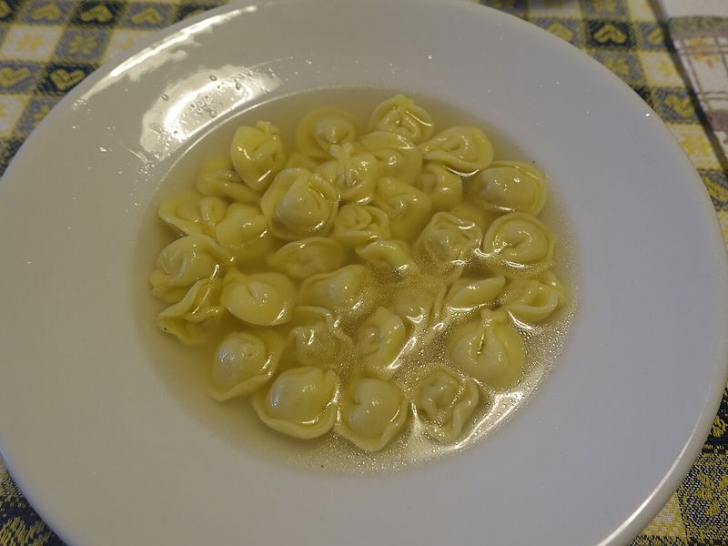 Prato fundo com tortellini pequenos boiando em caldo dourado.